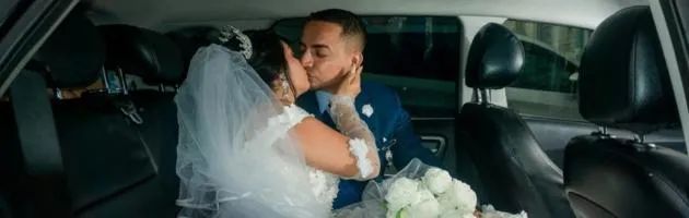Bride and groom kissing in a car on their wedding day, bouquet in foreground