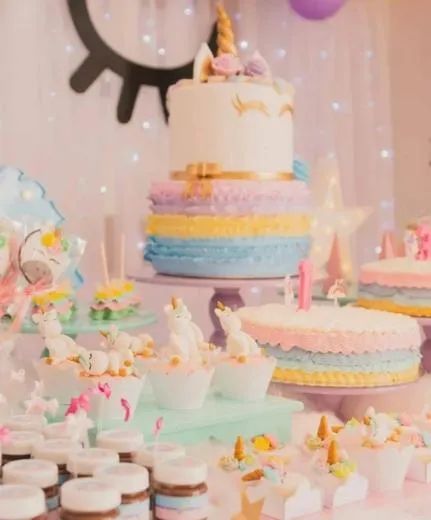 Pastel birthday dessert table with tiered cakes, cupcakes, and candles on a pink backdrop