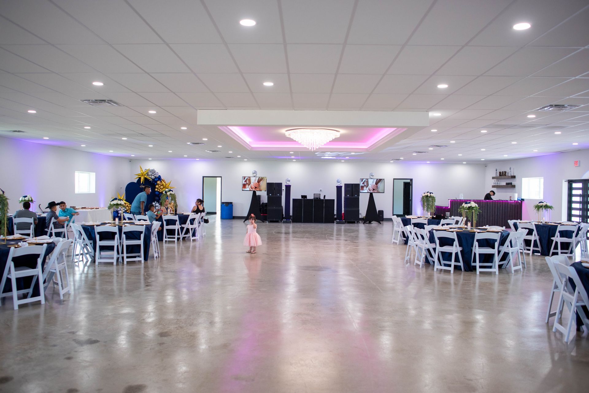 Large banquet hall with white tables and chairs, polished floor, and a decorated stage at the far end