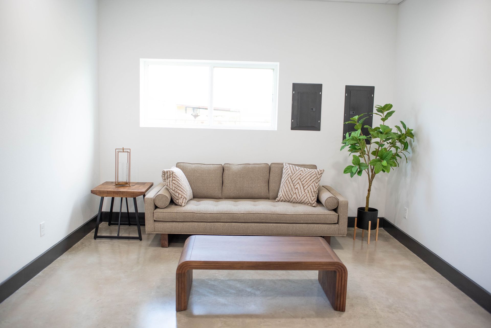 Minimal living room with beige sofa, wooden coffee table, side chair, and potted plant by a bright window.