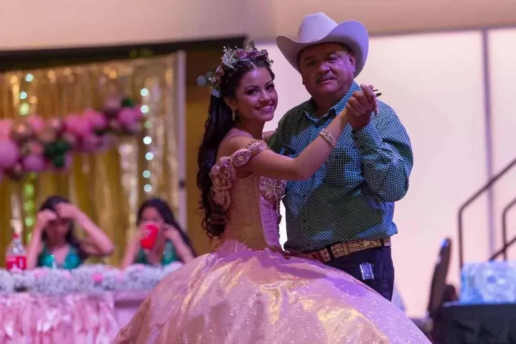 Couple dancing at a formal event, with the woman in a pink gown and the man in a cowboy hat.