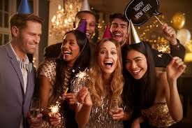 Friends smiling and holding sparklers at a festive indoor celebration with balloons and warm lights