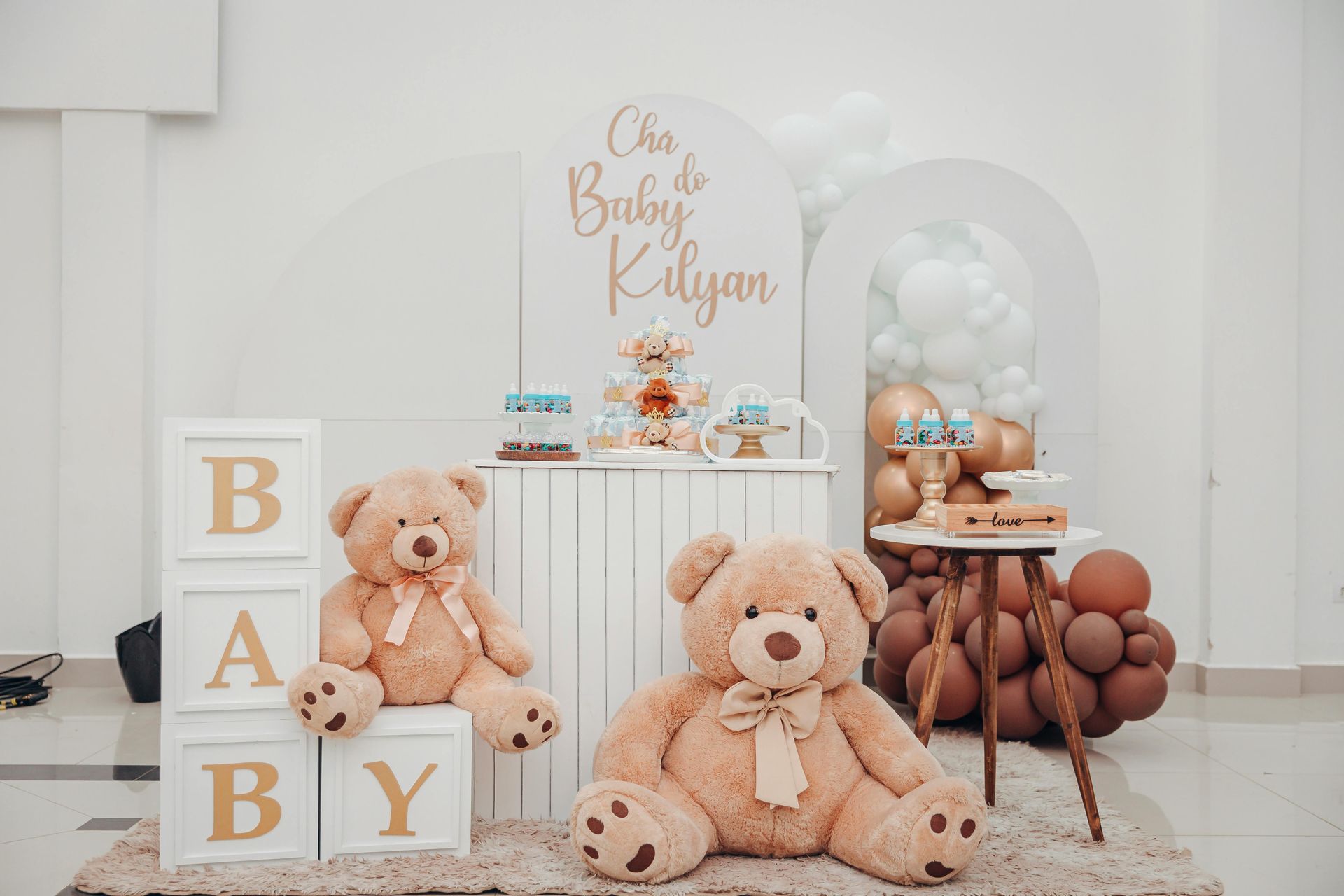 Baby shower setup with teddy bears, beige balloons, and a white cake table with “Baby” blocks.