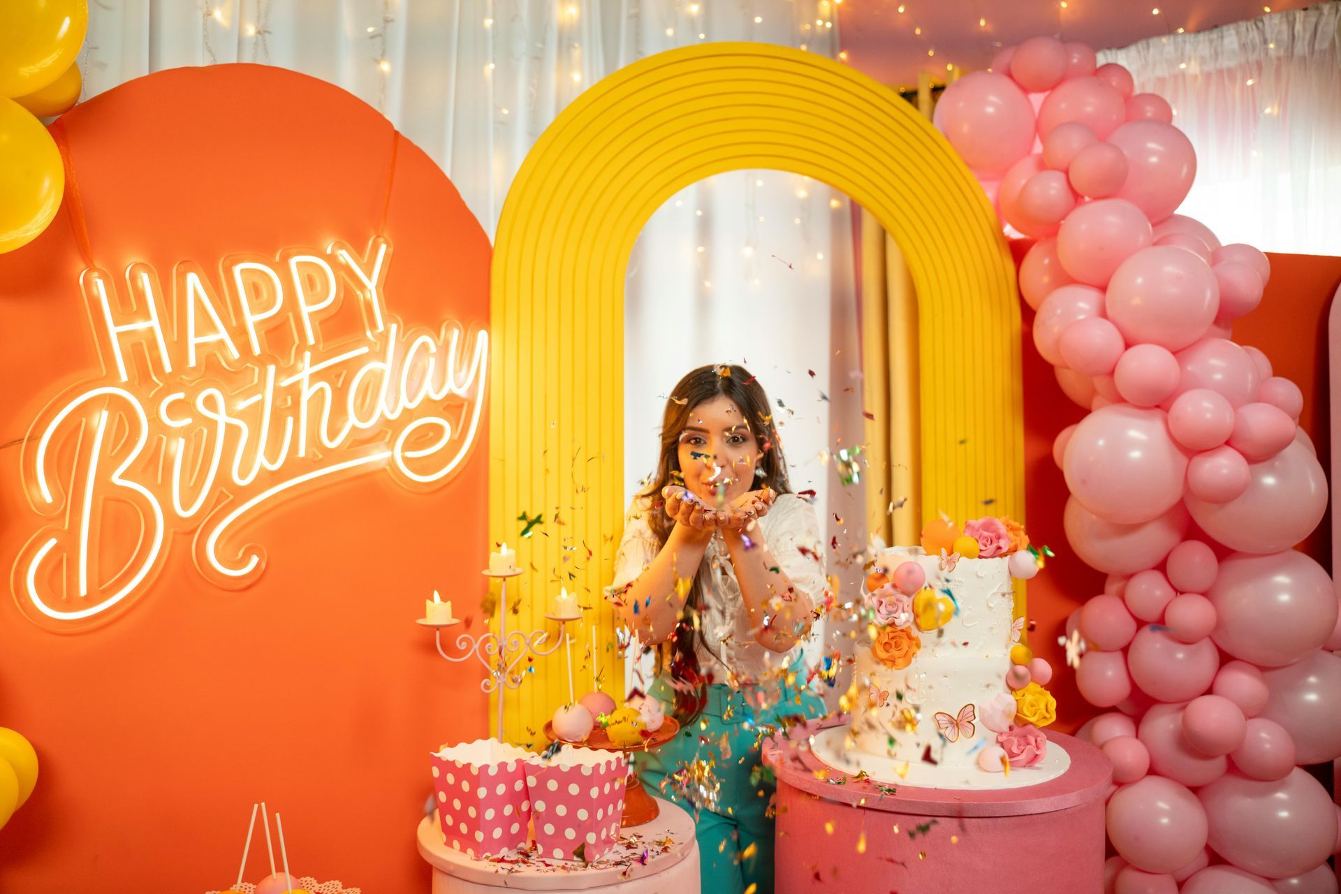 Child at a colorful birthday party with balloon arch, cake, confetti, and a glowing “Happy Birthday” sign