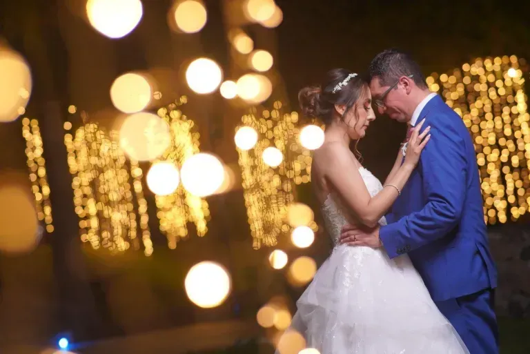 Couple in blue suit and white gown embracing at a bokeh-lit evening wedding