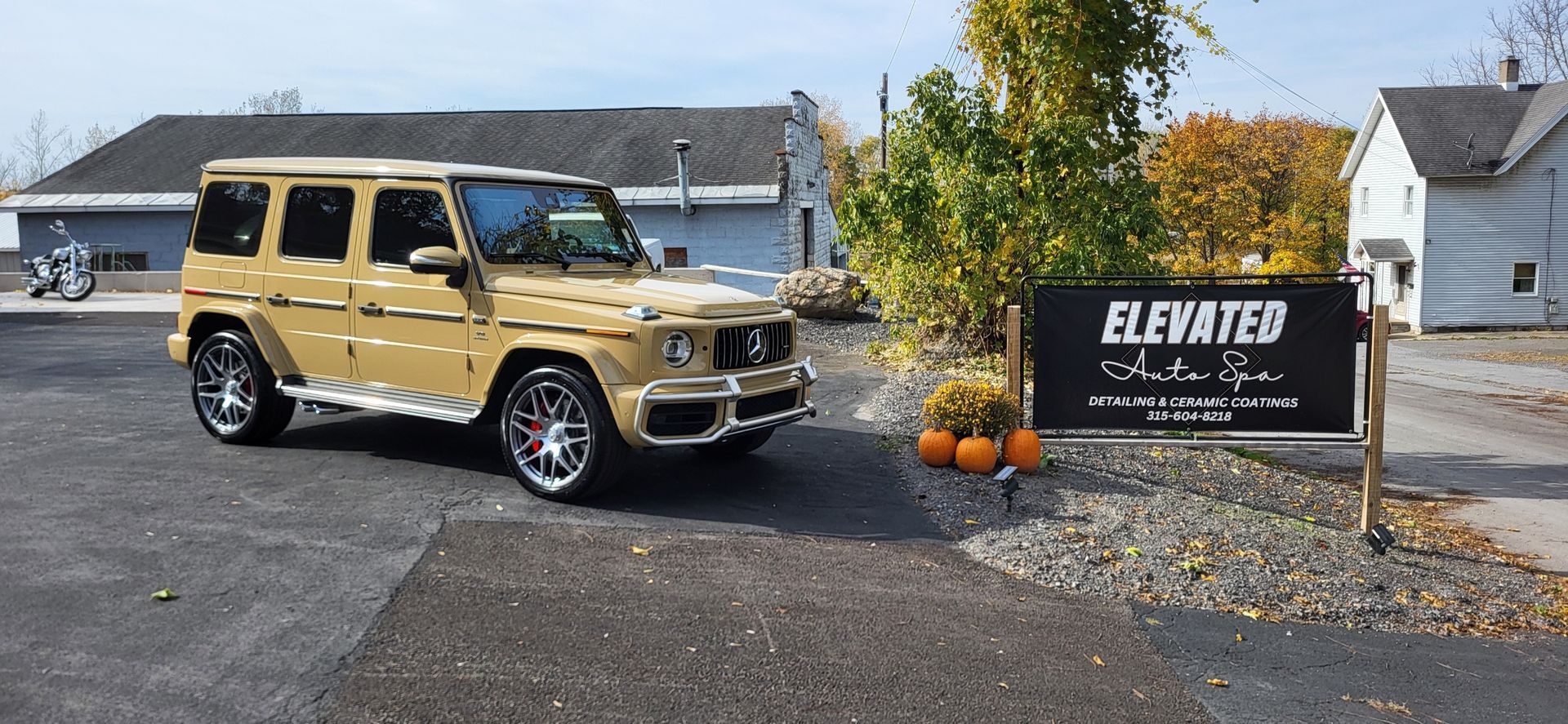 A gold mercedes benz g63 is parked in front of a sign that says elevated auto spa.