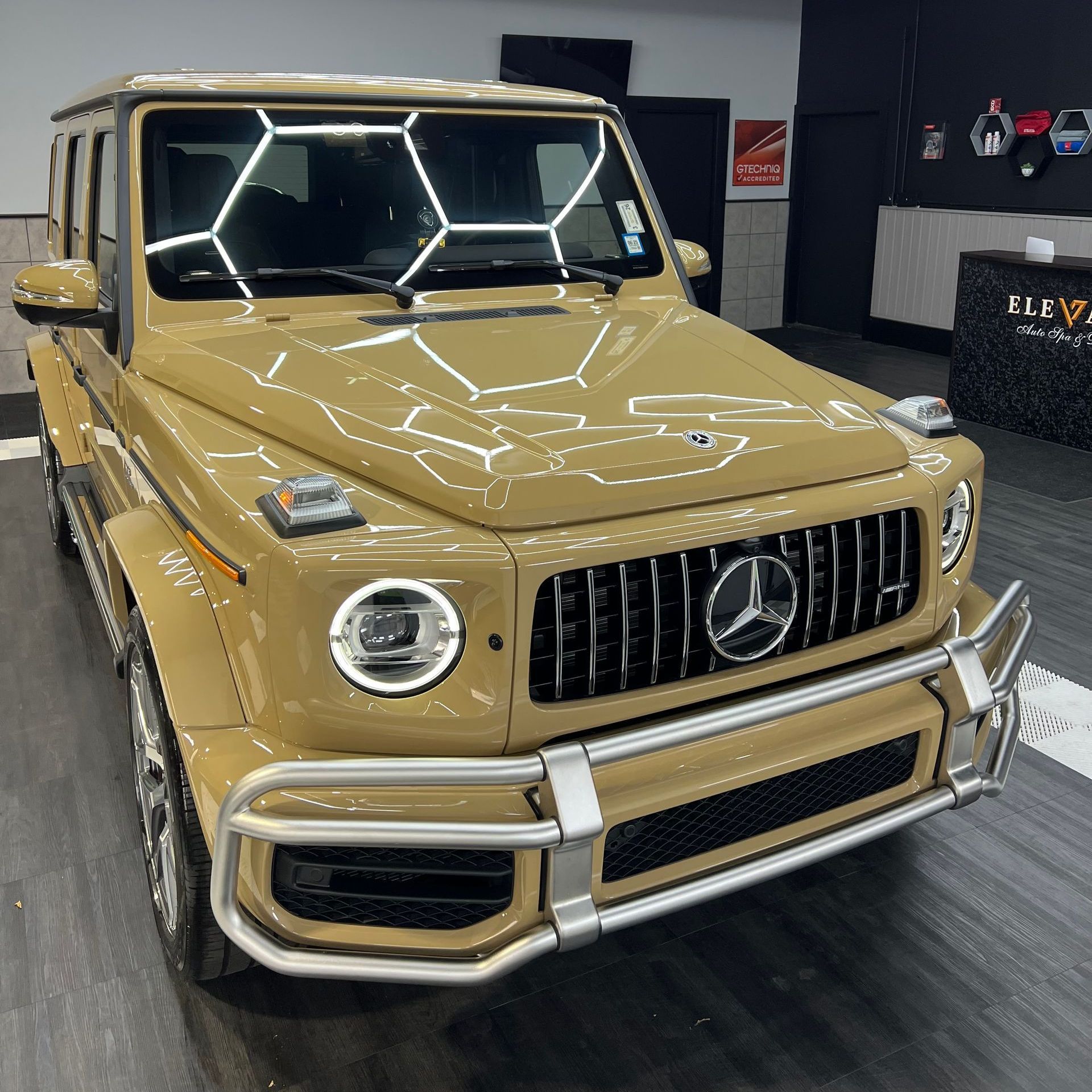 A tan mercedes benz g63 is parked in a showroom.