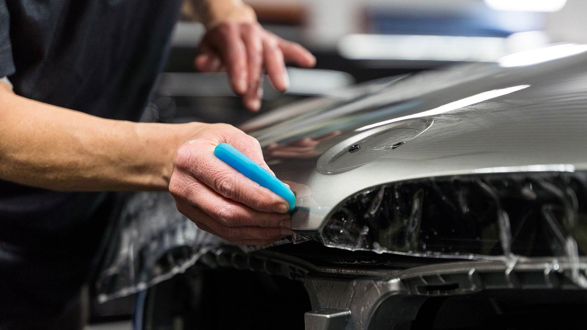 A man is applying a protective film to the hood of a car.