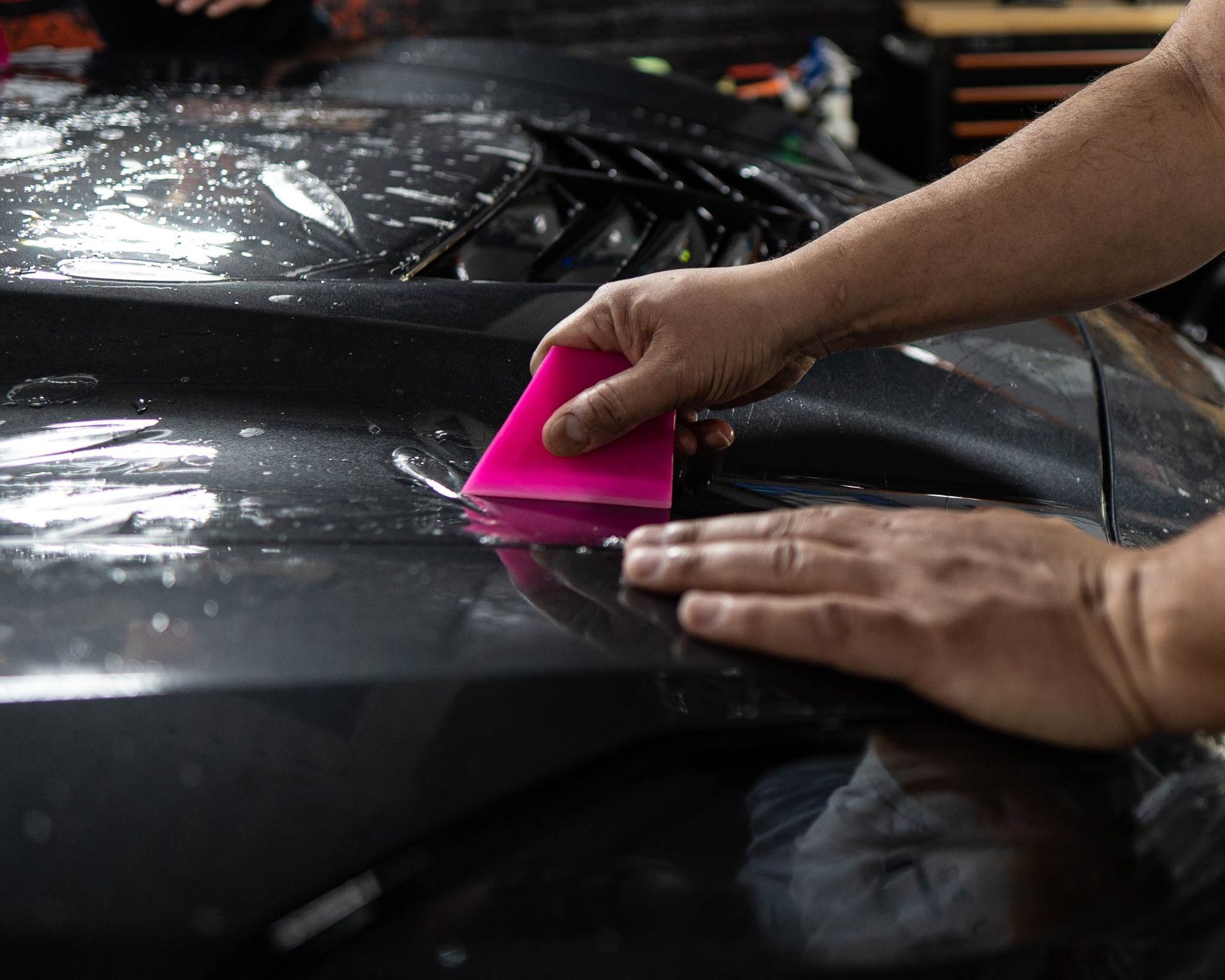 A person is wrapping a car with a pink squeegee.