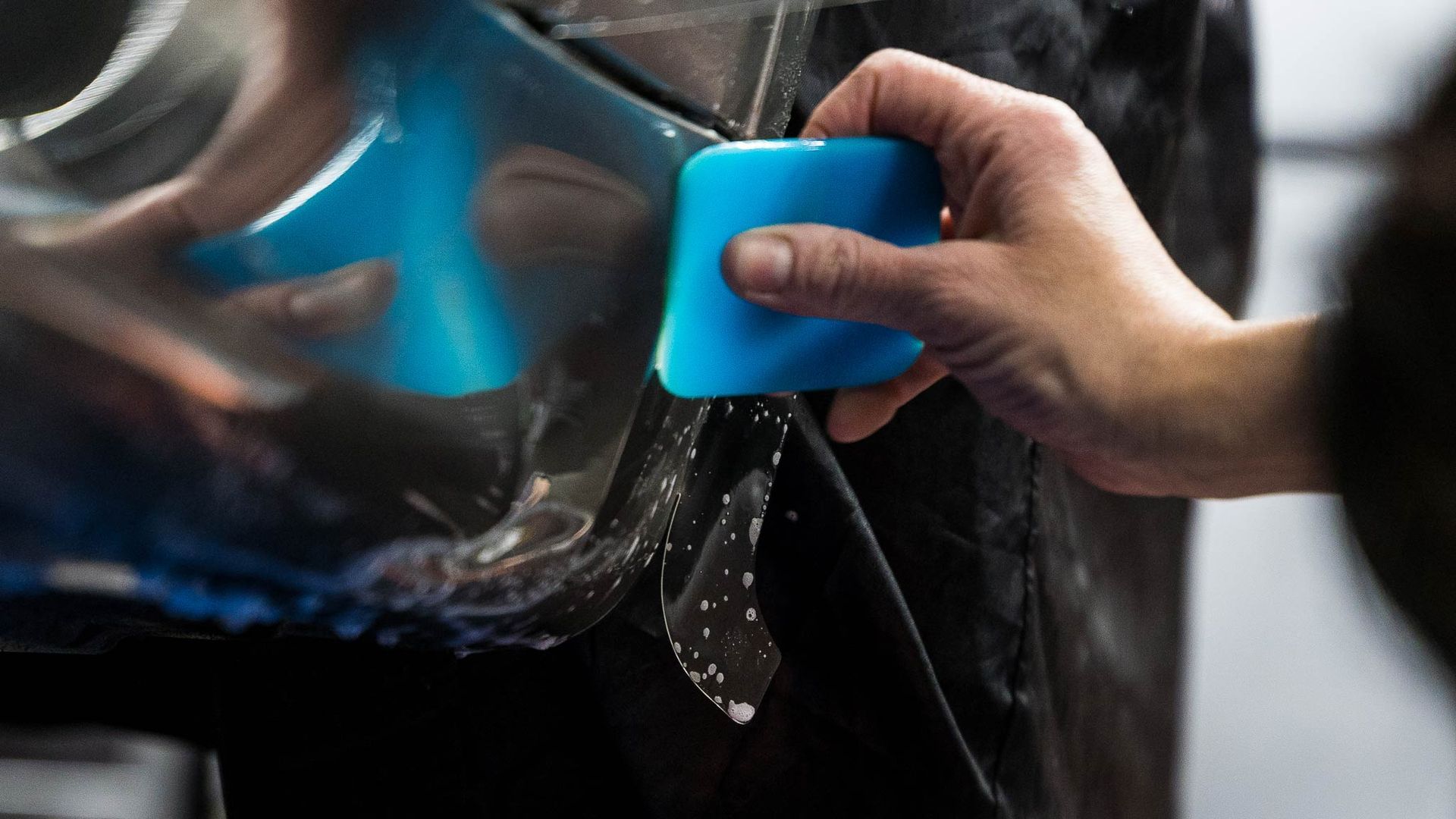 A person is applying protective film to a car with a blue spatula.