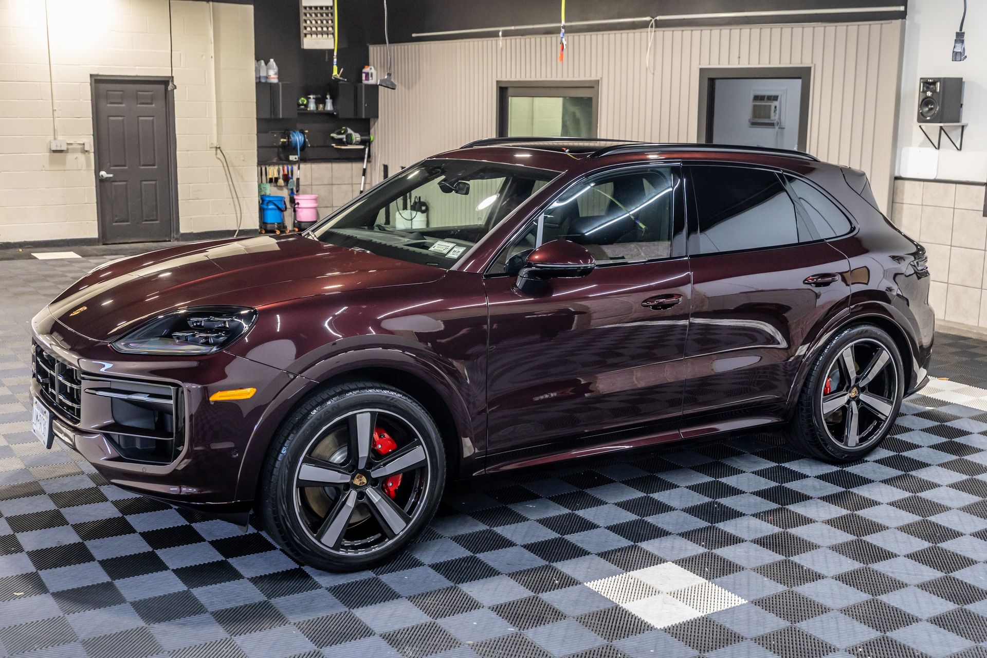 A red porsche cayenne is parked on a checkered floor in a garage.