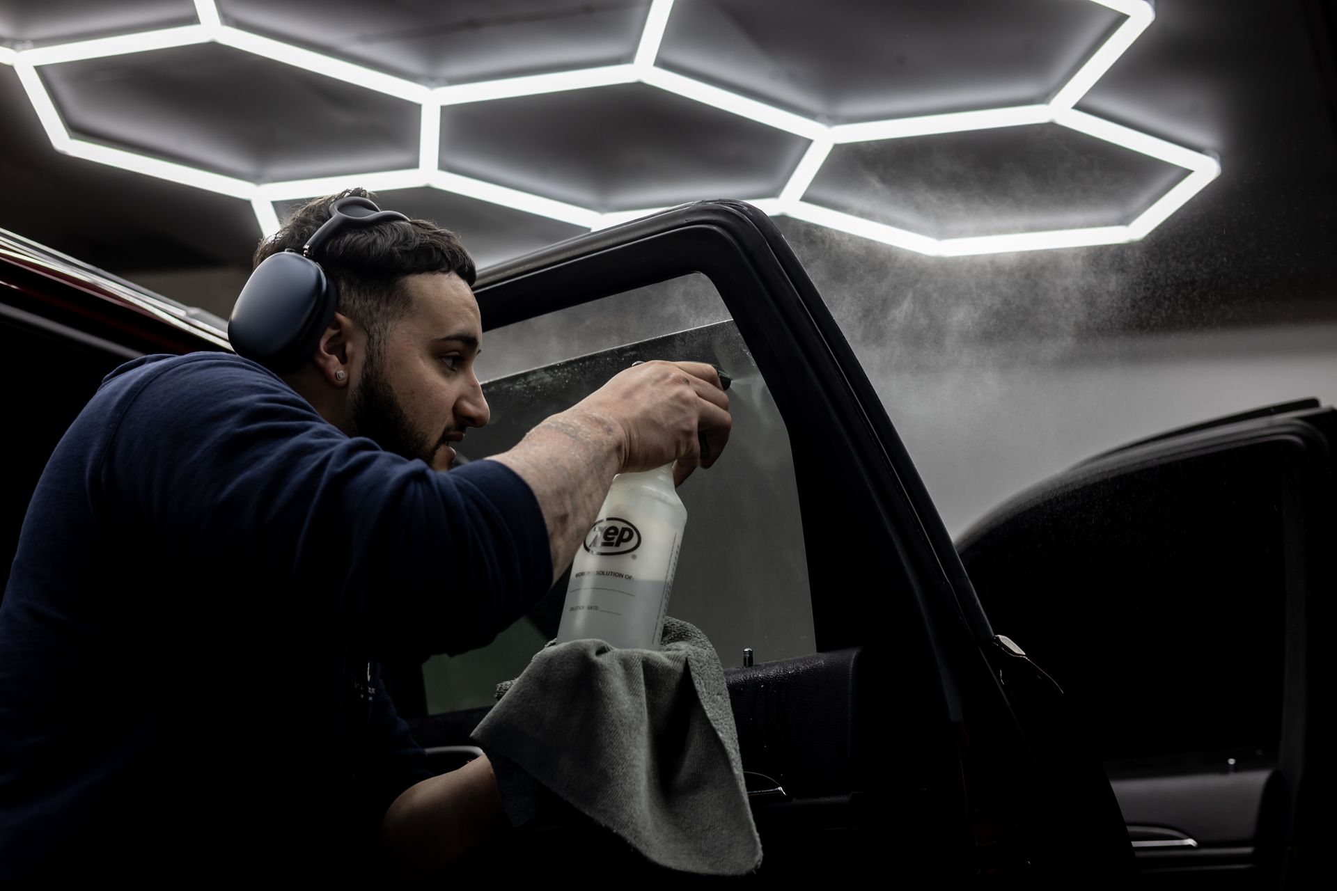 A man is spraying a car window with a spray bottle.