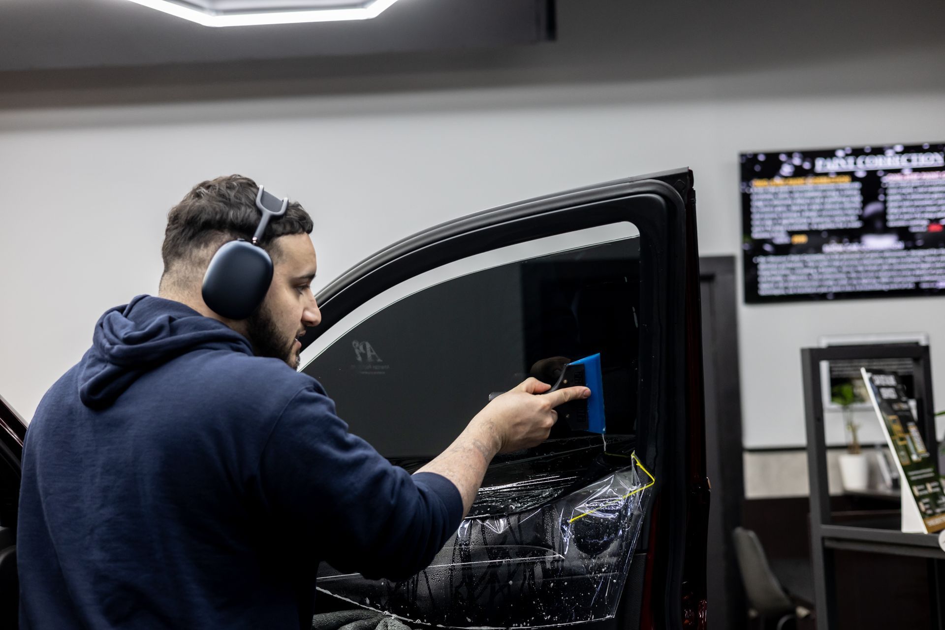 A man wearing headphones is applying window tinting to a car window.