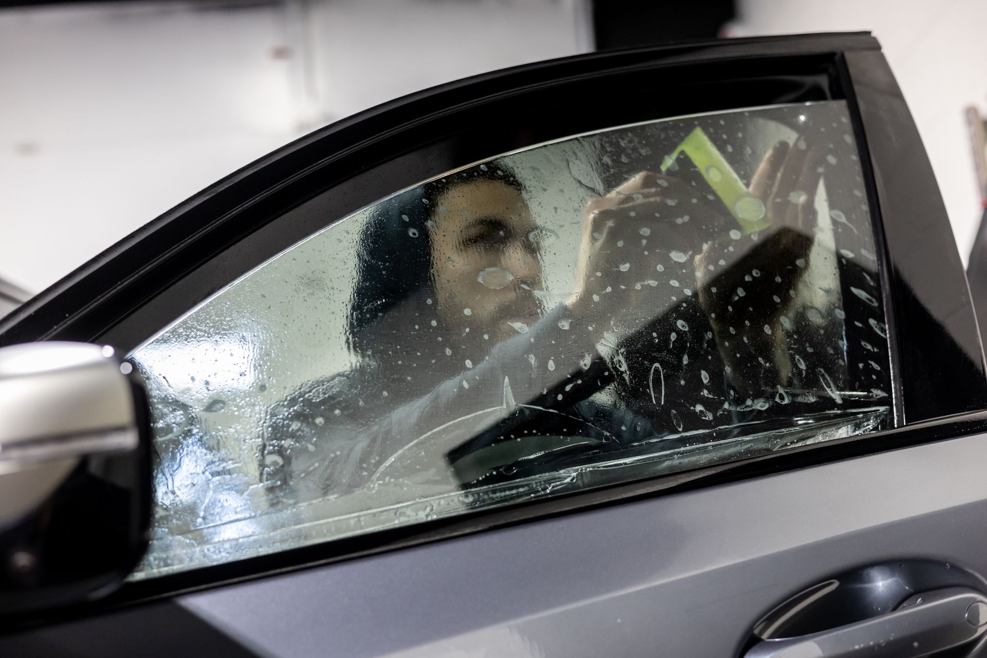 Person applying window tint to a car window, indoors, soapy water visible.