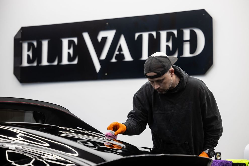 A man with a beard is cleaning the trunk of a car with a vacuum cleaner.