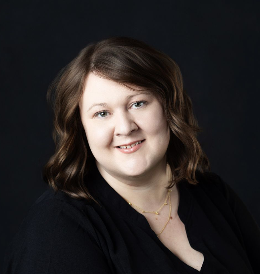 Woman with brown hair, smiling, wearing a black shirt, set against a dark blue background.