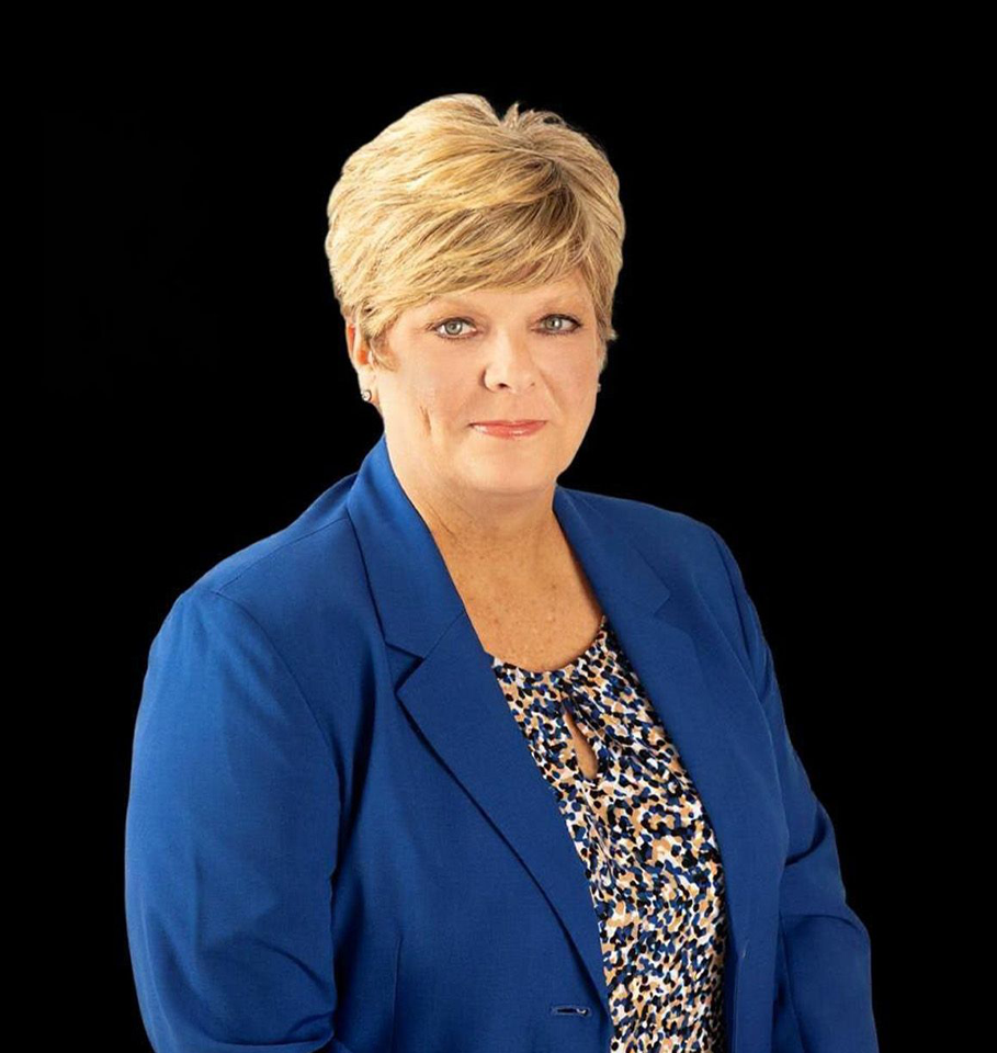 Woman in a blue blazer with short blonde hair against a black background.
