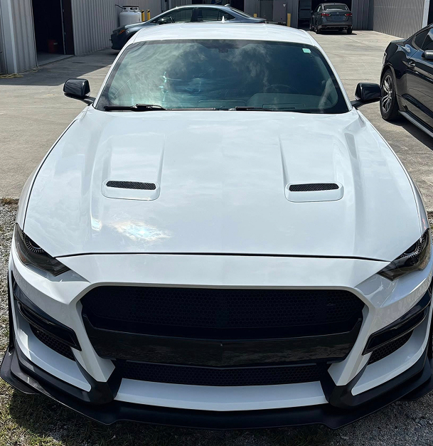 White Ford Mustang with black accents and hood vents, parked outside.