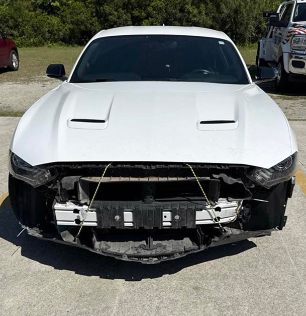 White Ford Mustang with front-end damage; bumper and grill are missing.