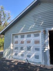Exterior view of a light green garage wall with a white garage door featuring taped-off window panels, mid-renovation.