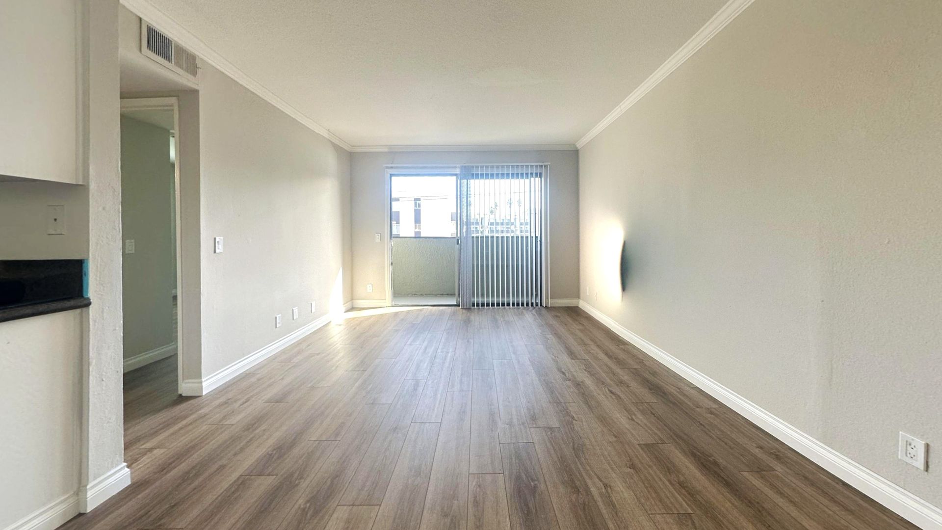 Empty living room with light-colored walls and wood-look flooring. Sliding door leads to a small balcony.