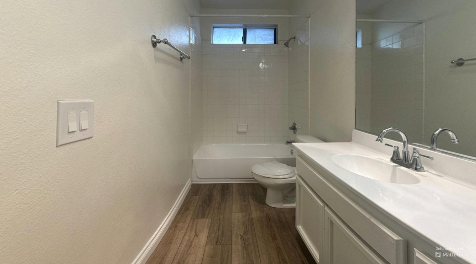 Bathroom with white walls, wood-look floor, white vanity with sink, toilet, and bathtub.