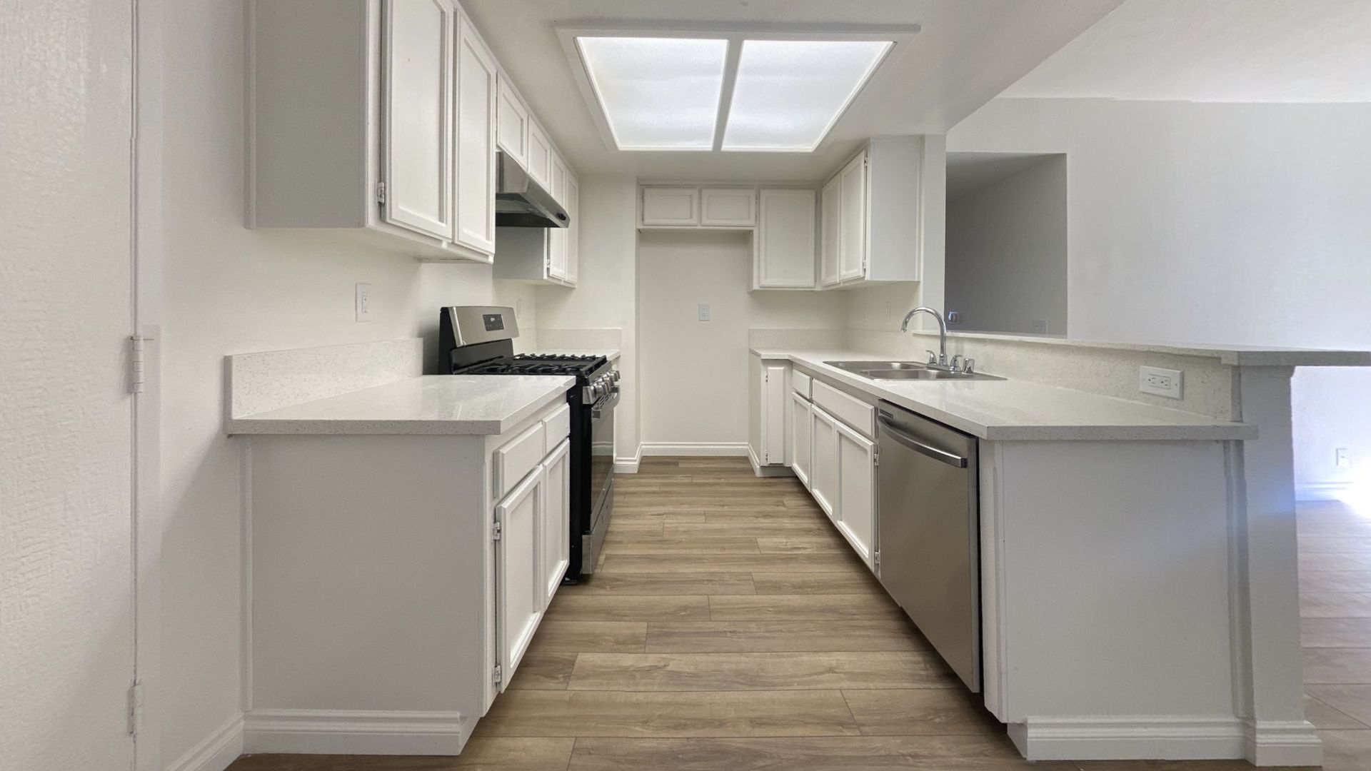 White kitchen with cabinets, countertops, stainless steel appliances, and wood-look flooring.