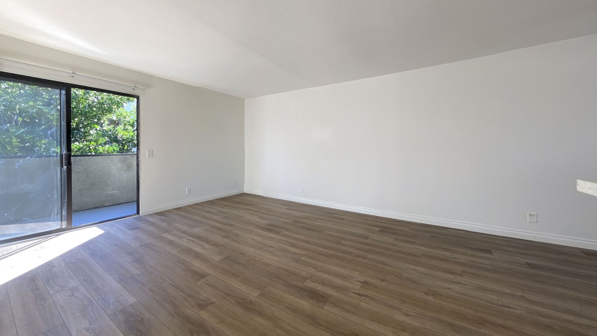 Empty room with wood-look floor, white walls, and sliding glass door leading to a balcony.