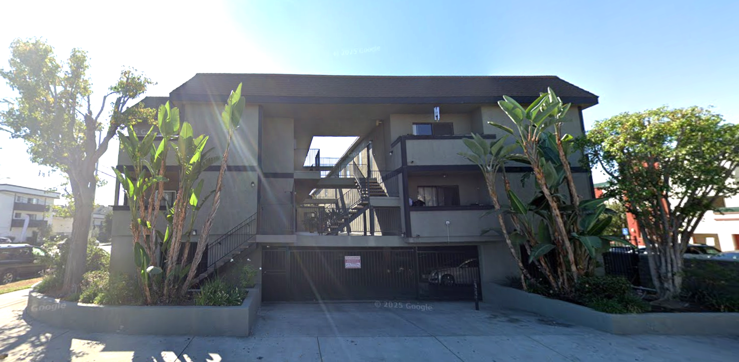 Apartment building with a dark entryway, surrounded by greenery and a sunny sky.