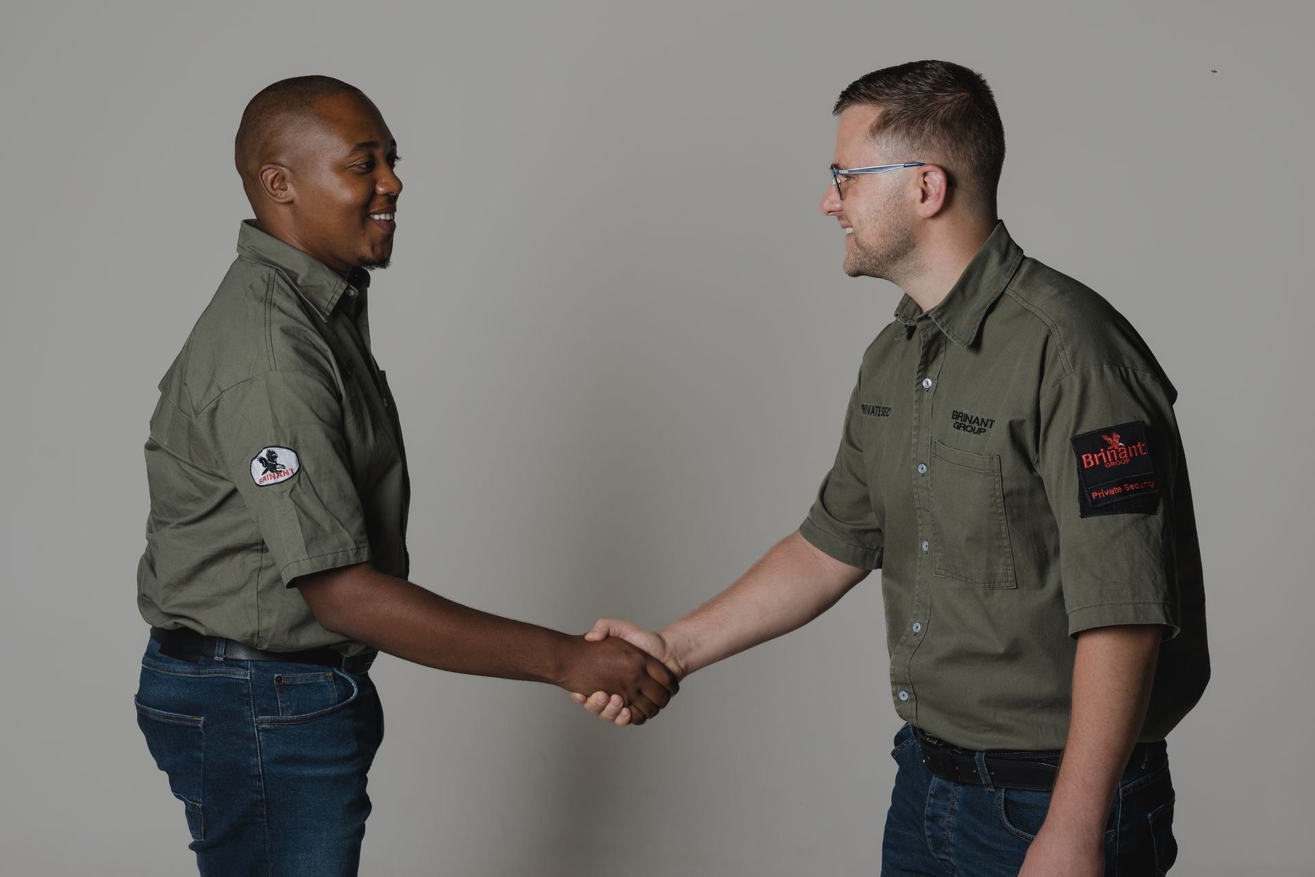 2 Brinant male employees, 1 black and 1 white, shaking hands whilst looking at each other.