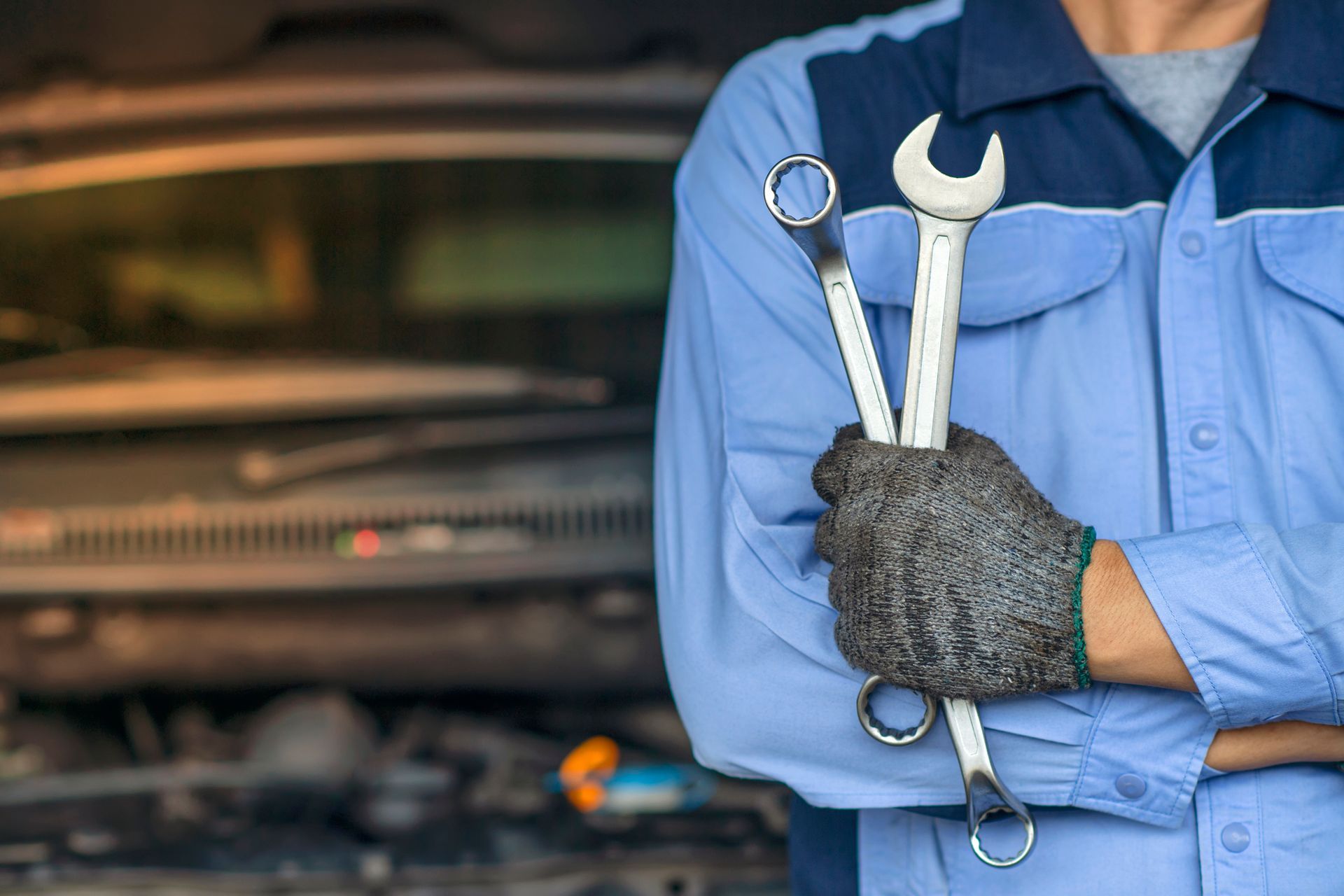 A mechanic is holding two wrenches in front of a car.