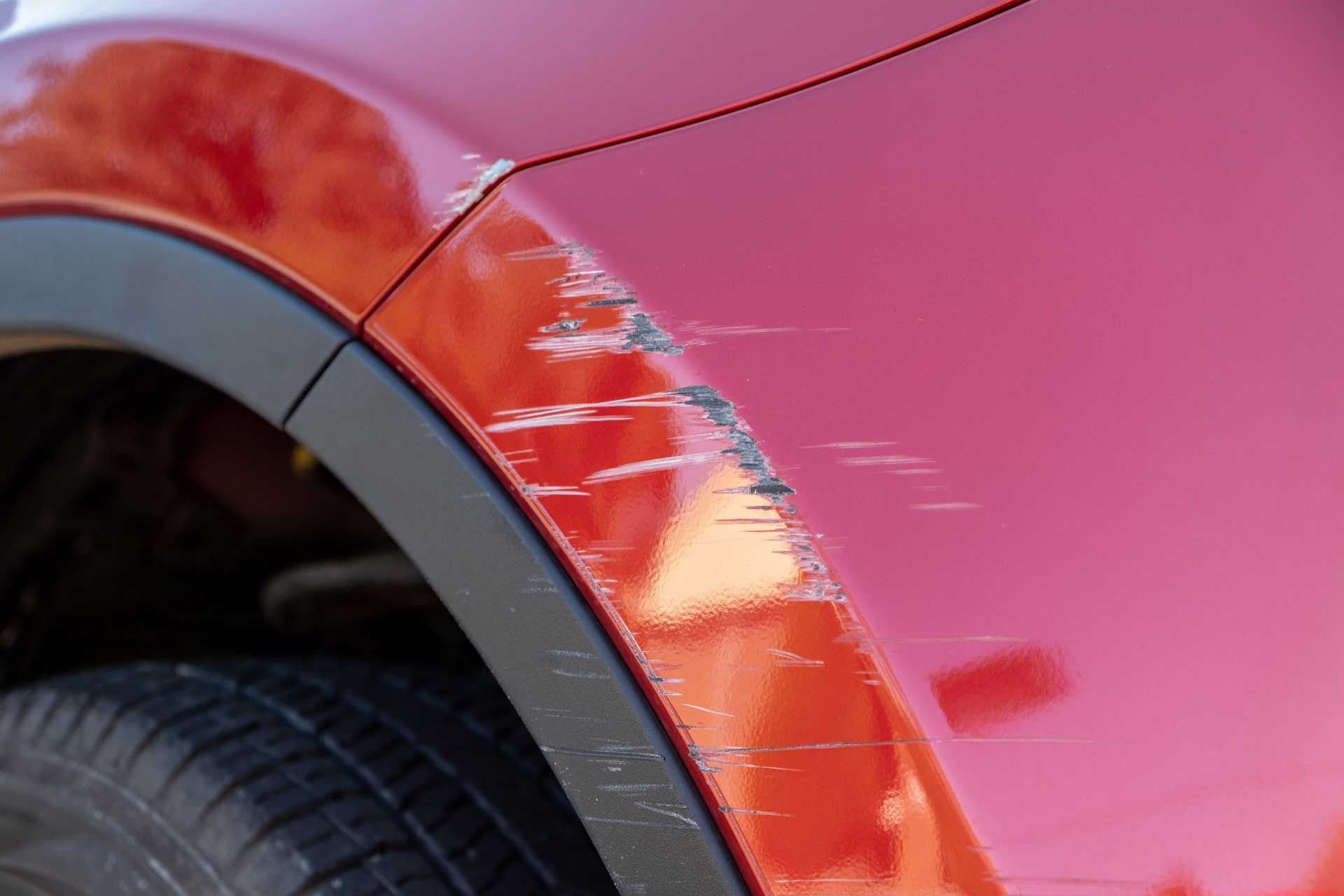 A close up of a red car with scratches on the fender