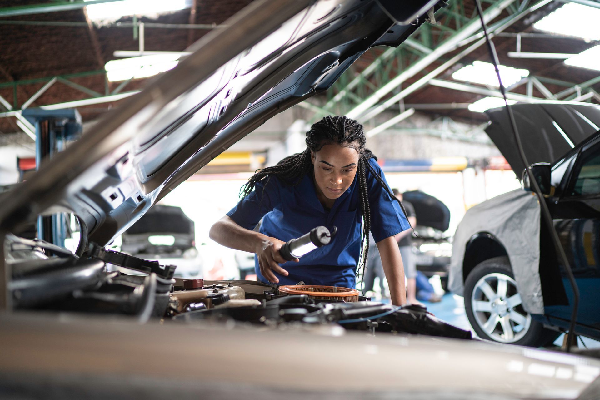 A woman is working on the engine of a car in a garage.