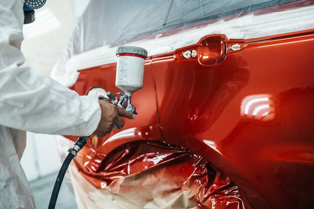 Spray painting a red car in the booth