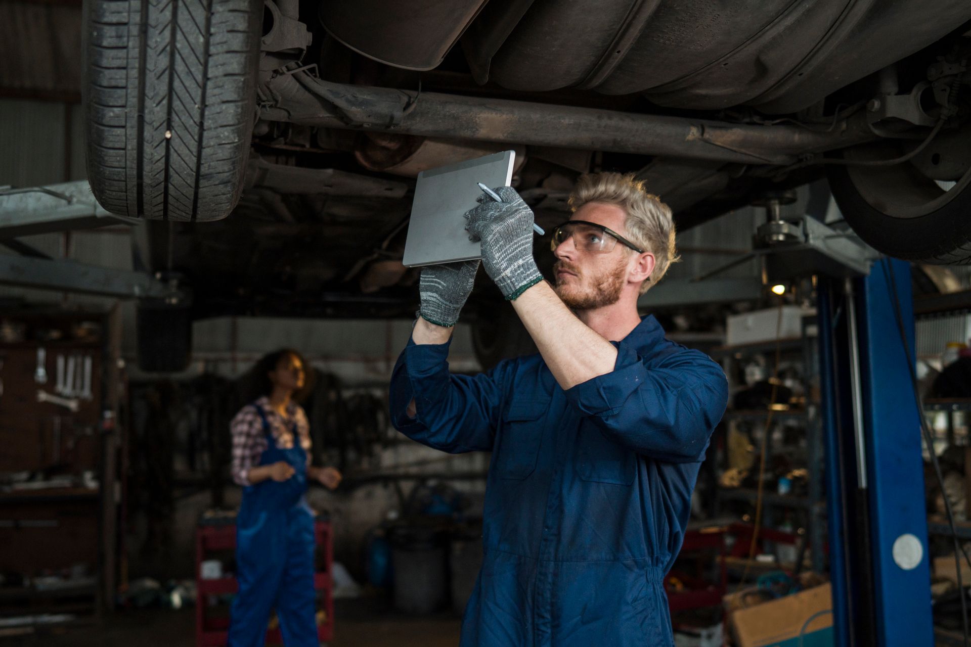 A mechanic is using a tablet under a car in a garage.