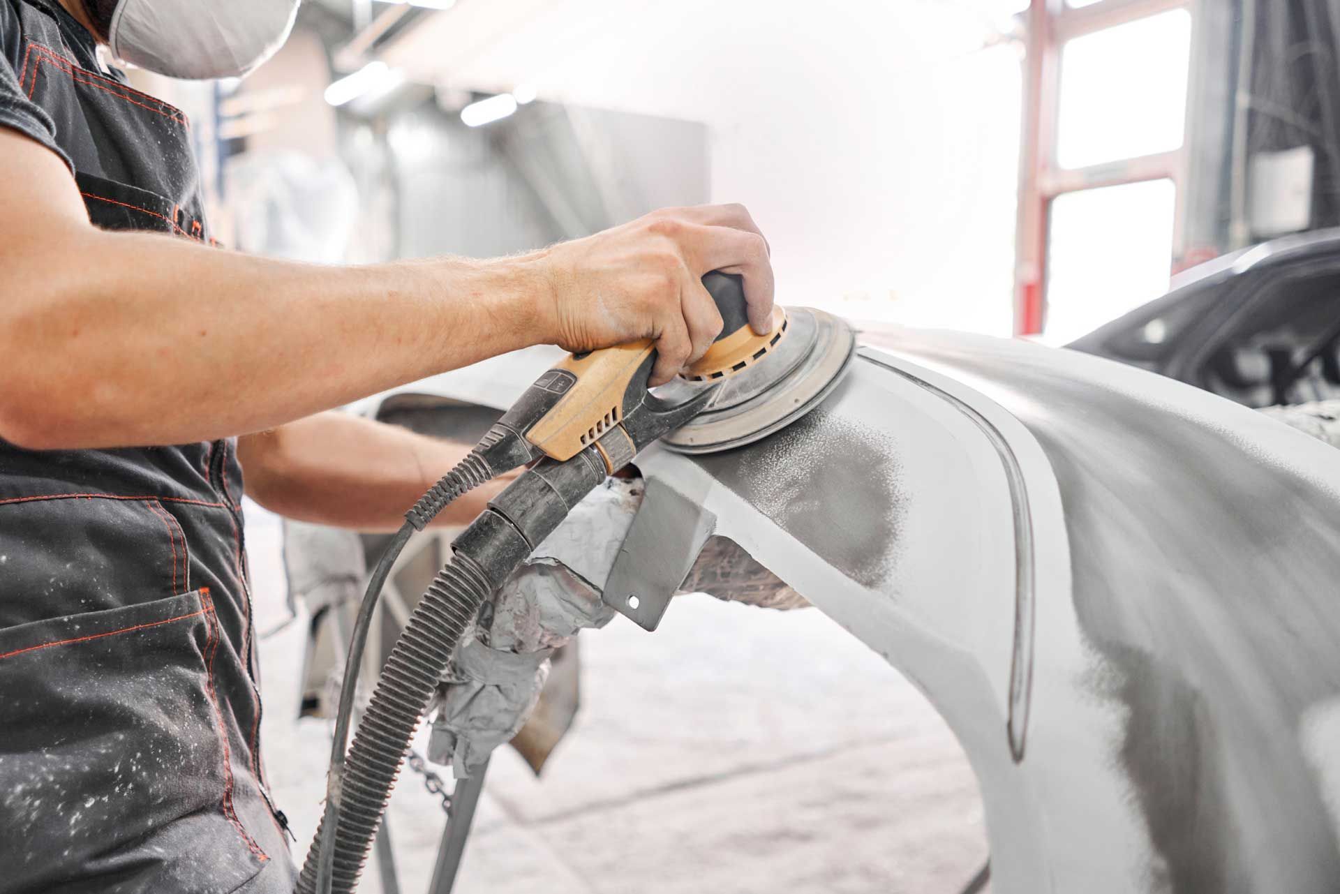 A man is sanding a car with a sander in a garage.
