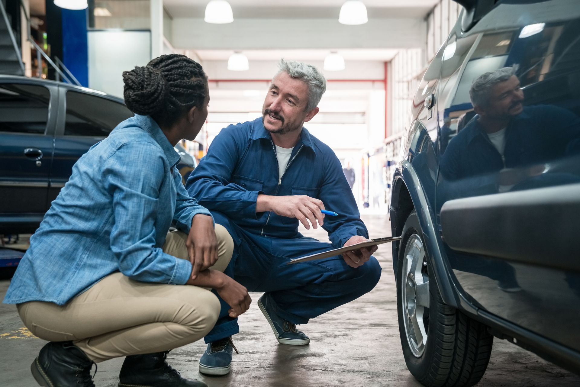 A man and a woman are looking at a car in a garage.