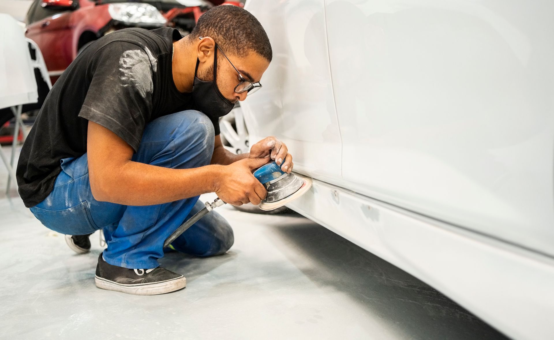 A man wearing a mask is working on a car in a garage.