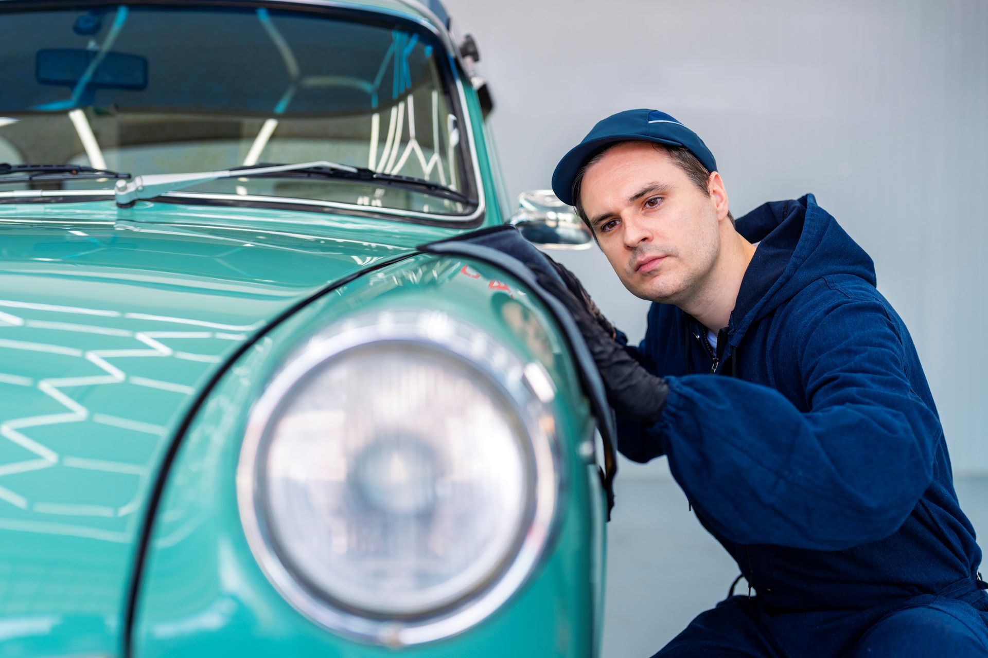 A man is polishing a green car in a garage.