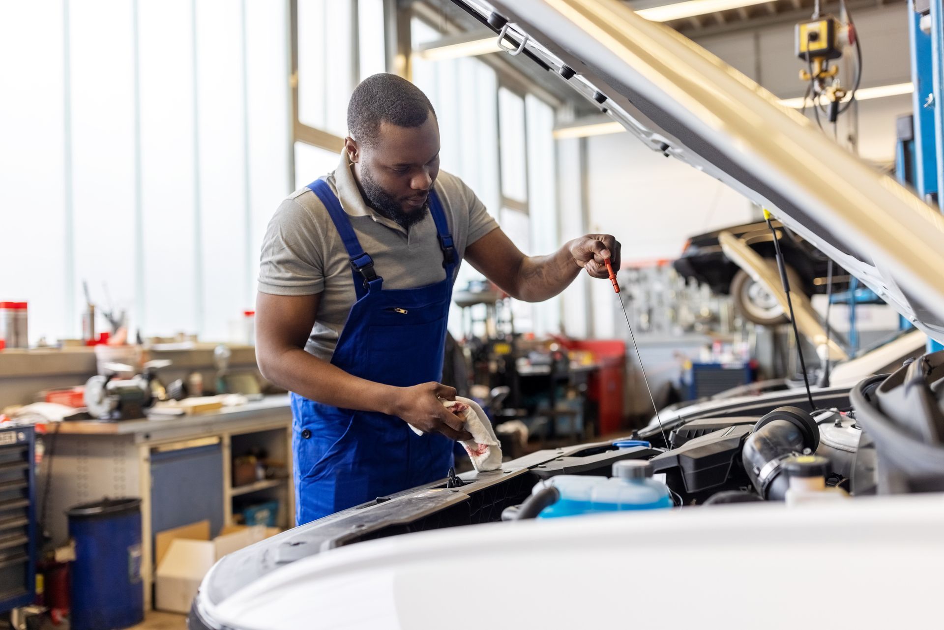 A man is working on a car in a garage with the hood open.