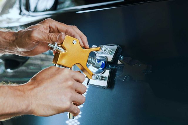 Technician using a tool to remove a dent from a car