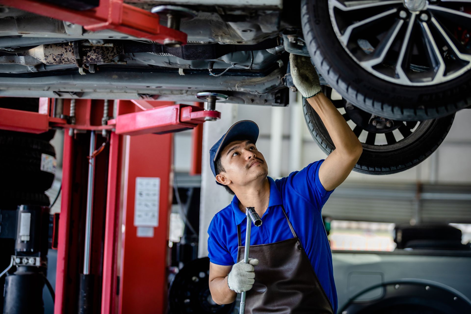 A man is working on the underside of a car in a garage.
