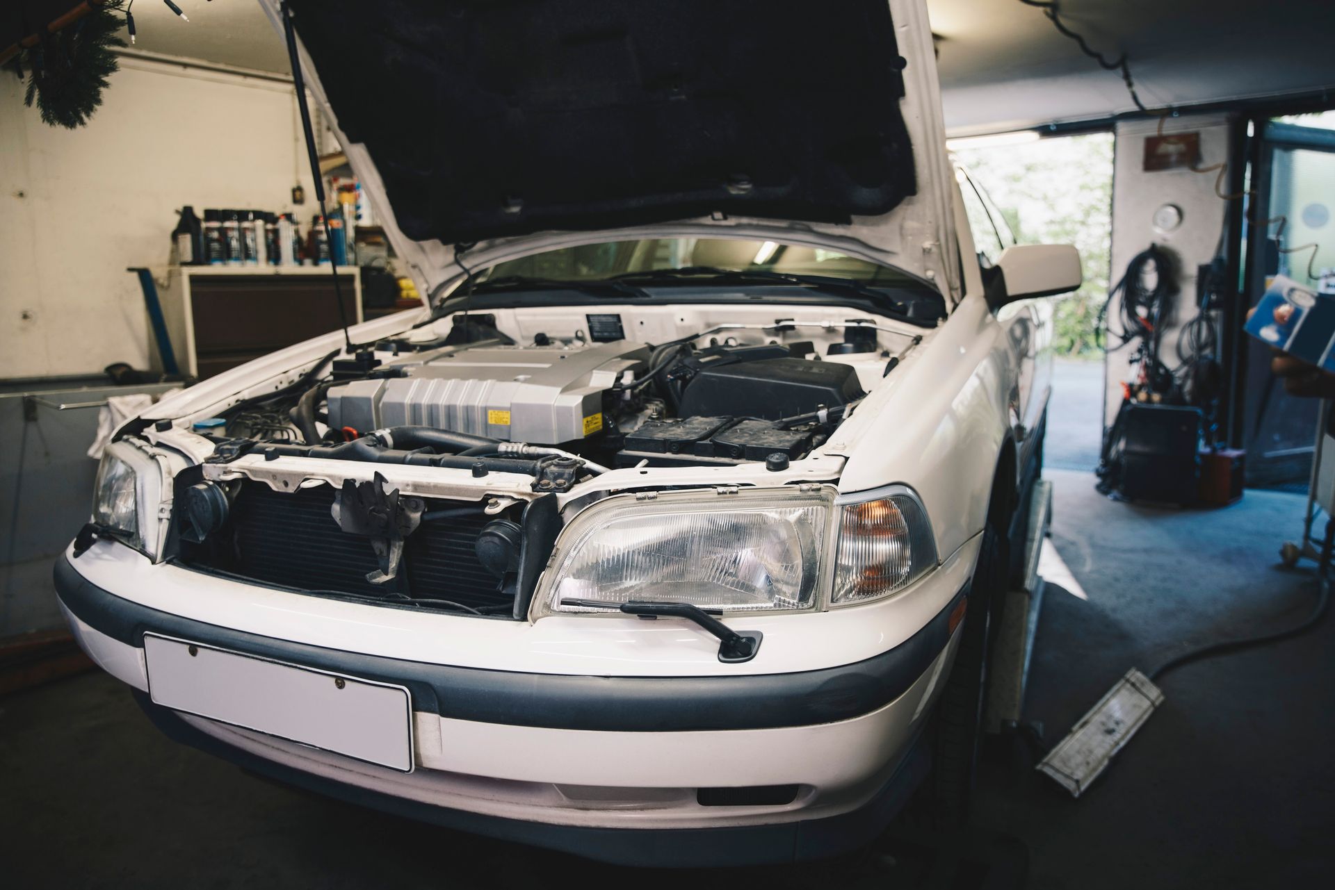 A white car with the hood open is sitting in a garage.