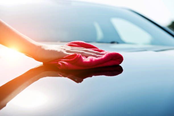 A person is cleaning the hood of a car with a towel.