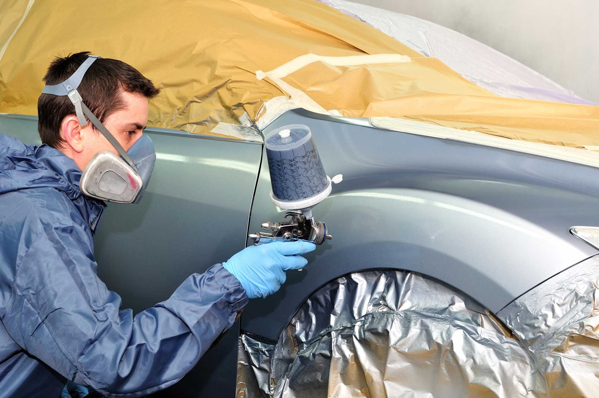 A man wearing a mask and gloves is spray painting a car.