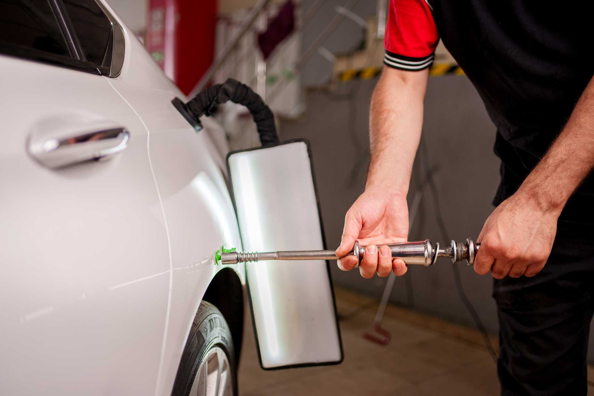 A man is using a hammer to fix a dent in a car.