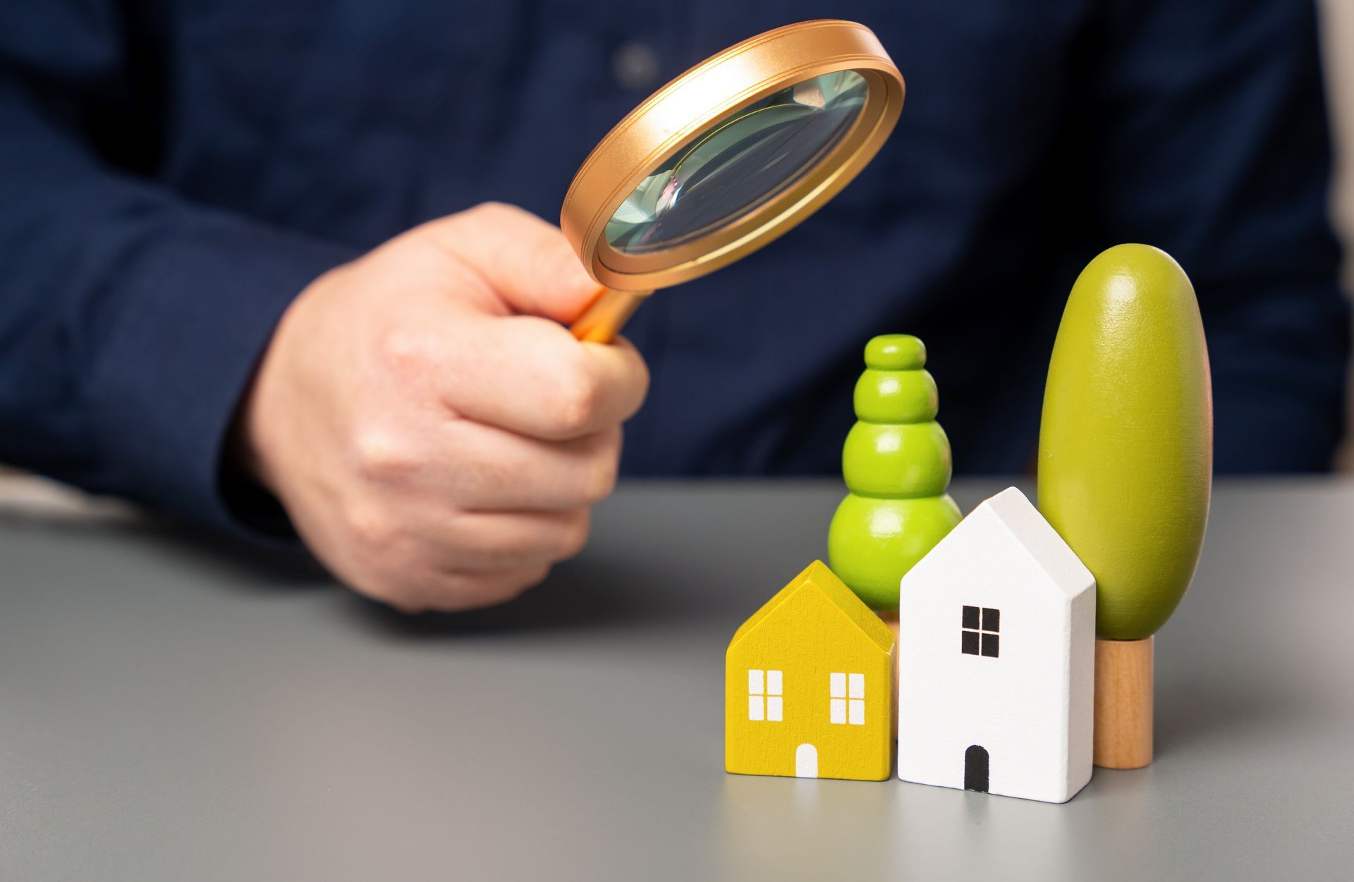 A person is holding a magnifying glass over a toy house.