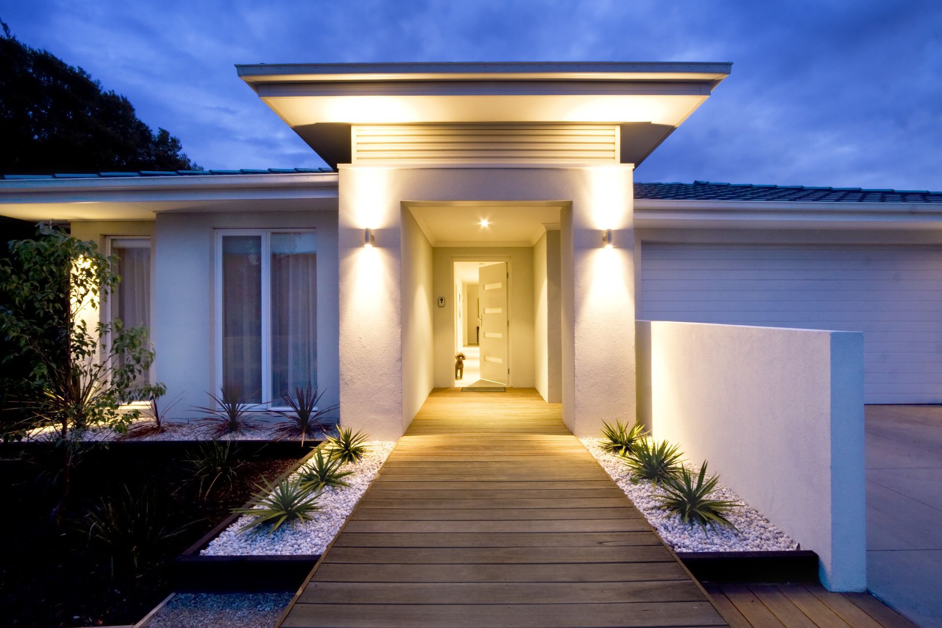 Modern house entrance with warm lights and a wooden walkway at dusk