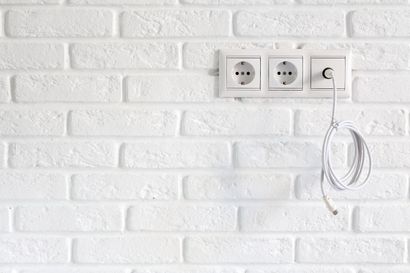 White brick wall with a three-socket outlet and a hanging cable loop