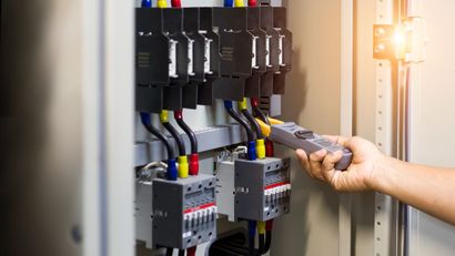 Technician testing electrical panel with a multimeter, with circuit breakers and wiring visible